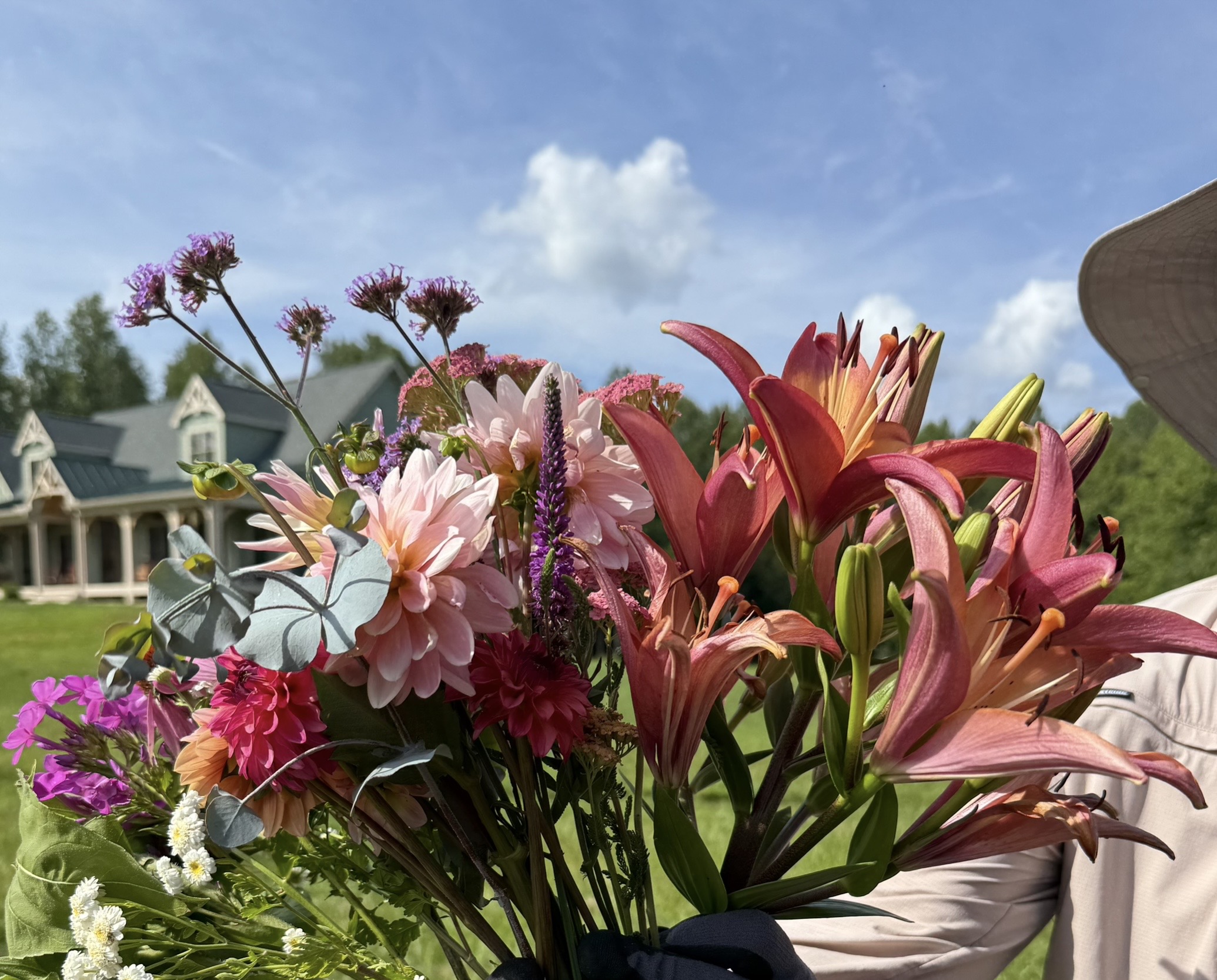 A hand-tied bouquet of farm-grown flowers held in front of the farmhouse